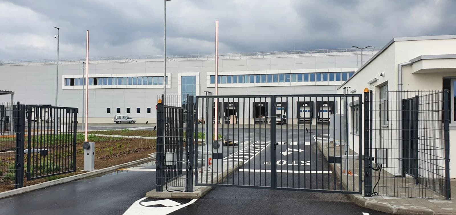 Siva dvokrilna metalna kapija sa podignutom parking rampom ispred industrijske hale.