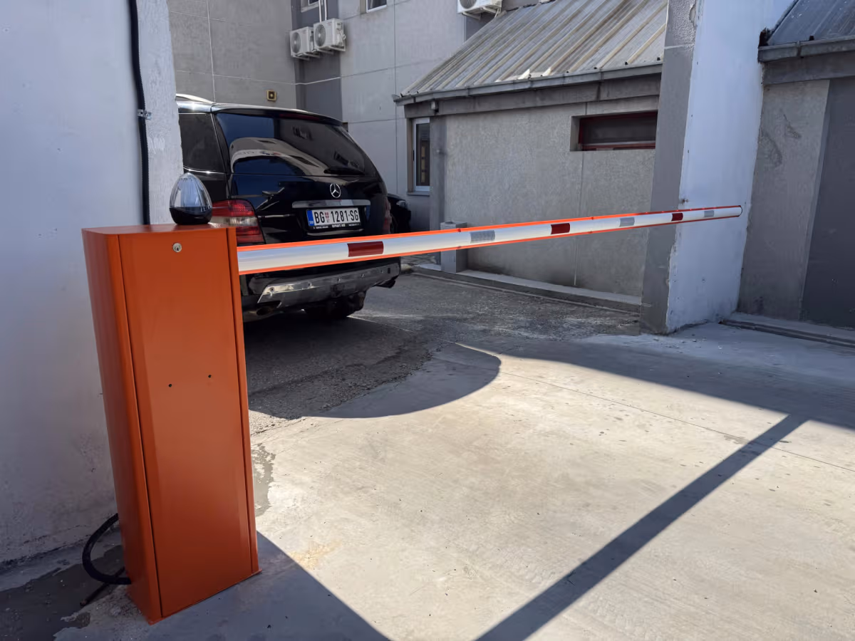 Narandžasta parking rampa sa crveno-belom rukom ispred parkiranog automobila.