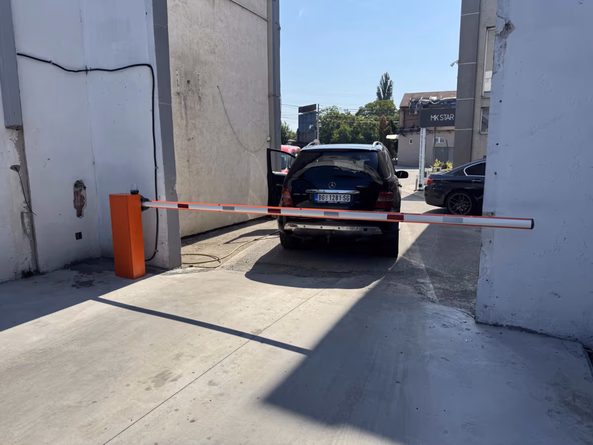 Narandžasta parking rampa sa spuštenom crveno-belom rukom preko prolaza između objekata.